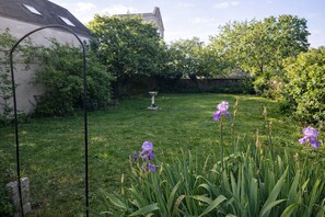 A garden with a lawn, a birdbath, and purple flowers.
