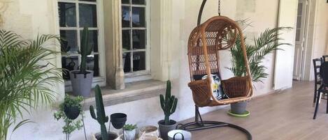 A wicker hanging chair with cushions, potted plants, and a patterned rug on a wooden floor.