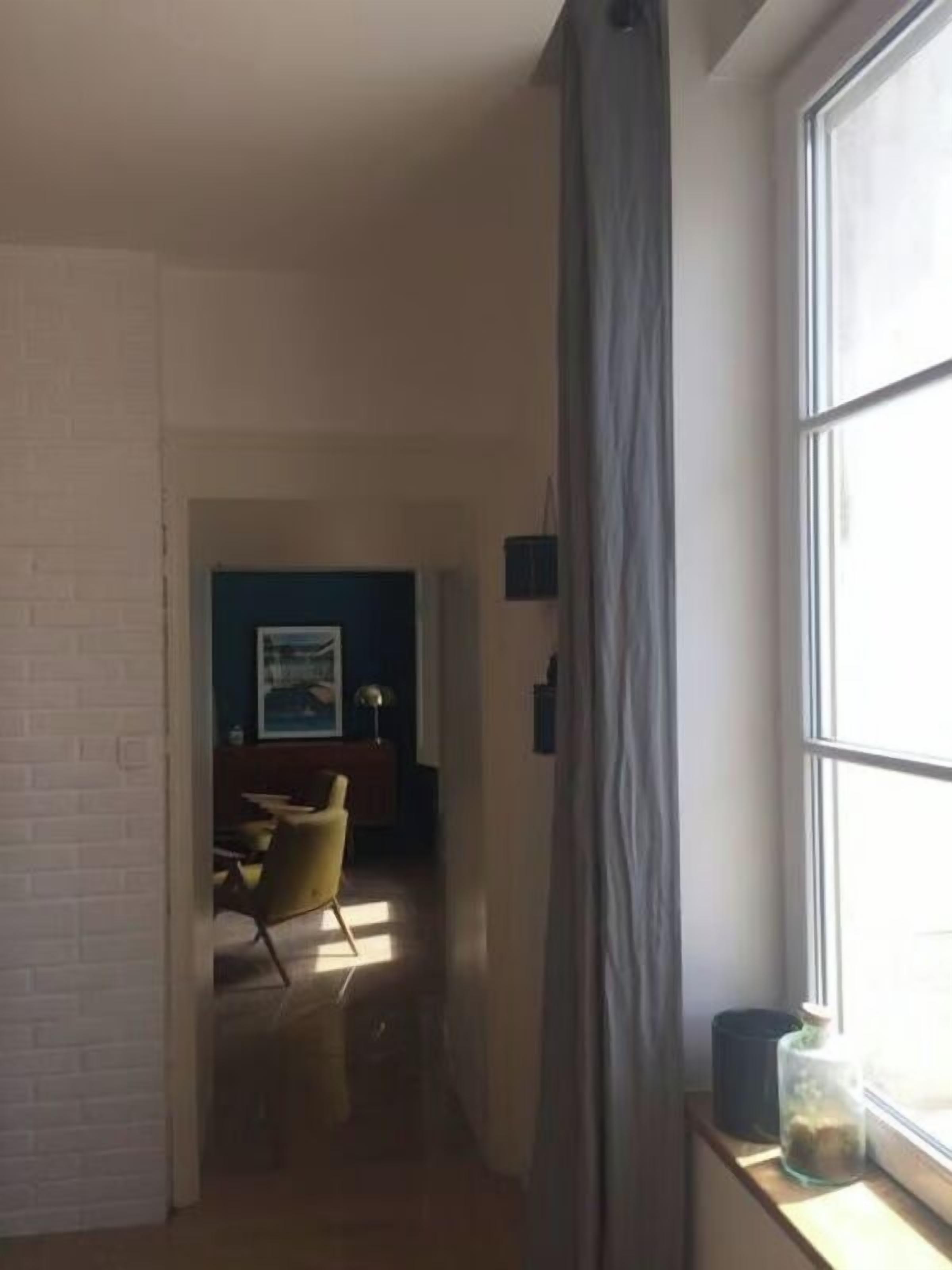 Ein schmales Gang mit einem Fenster auf der rechten Seite, der zu einem Essbereich mit einem Stuhl und einem Tisch führt.