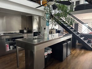 A modern kitchen with stainless steel appliances, a central island, and a staircase leading to an upper level.