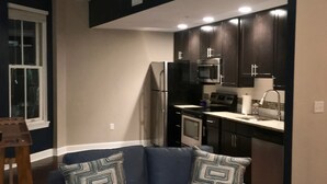 A living room with a dark blue sofa, patterned cushions, and a wooden coffee table. A kitchen with dark cabinets and stainless steel appliances is visible in the background. - "Market View" 2Br, 2ba, Best view of the Market Square, Great Location (Knoxville)