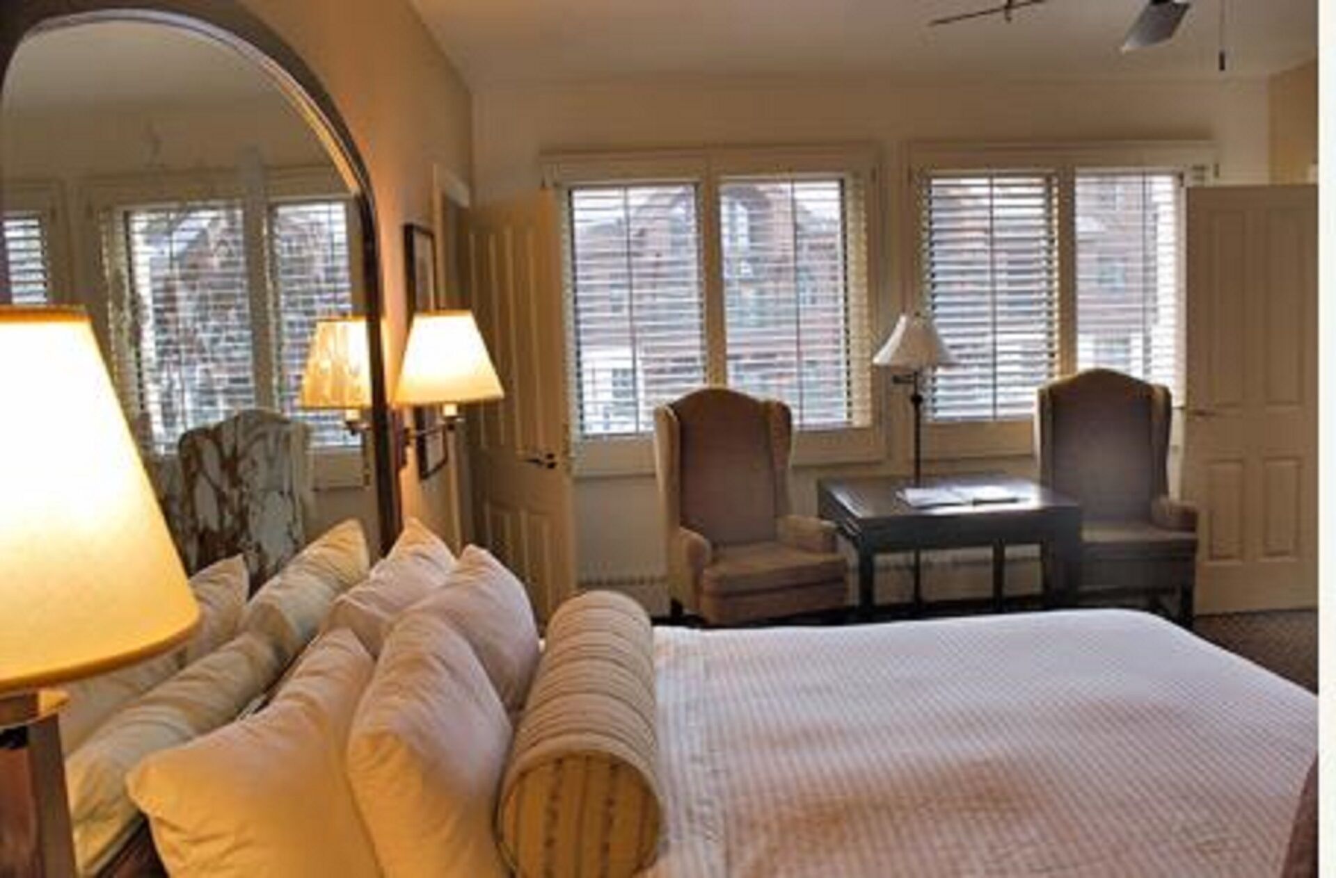 A hotel room with a large bed, two armchairs, a small table, and a mirror.