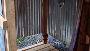 Eine Holzterrasse führt zu einer Metalttür mit einem kleinen Fenster, umgeben von Kies und Holzdielen.