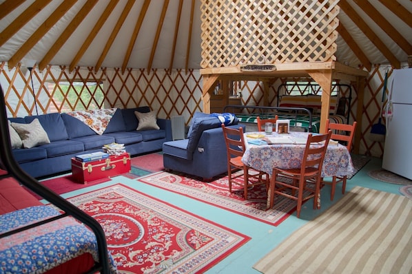 L’intérieur chaleureux d’une yourte, avec un canapé bleu, une petite table entourée de chaises et une valise rouge.