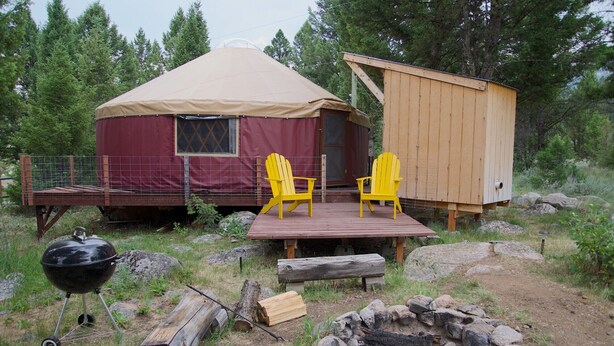 Eine Jurte mit einer Holzterrasse, zwei gelben Stühlen, einem Grill und einem kleinen Holzbau.
