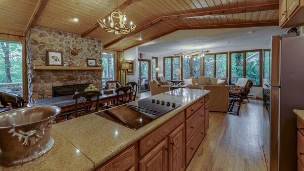 A spacious kitchen with a stone fireplace, wooden ceiling beams, and large windows offering views of the outdoors.