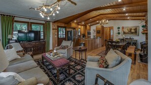 A spacious living room with a large television, wooden furniture, and a chandelier.