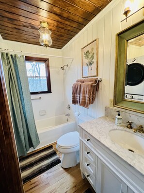 Une salle de bain avec un plafond en bois, une baignoire, des toilettes, un lavabo avec un plan de toilette en marbre et un miroir.
