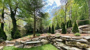 A stone wall with a sign, surrounded by green grass and trees.