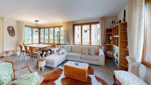 A spacious living room with a large window, a sofa, a wooden coffee table, and a dining area with a table and chairs. - Popular and centrally located residential building in St. (St. Moritz)