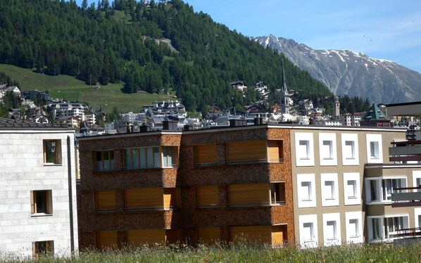 A multi-story building with a brick facade and multiple windows, set against a backdrop of a mountainous landscape. - Popular and centrally located residential building in St. (St. Moritz)