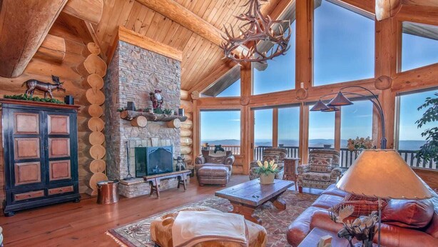 Amplia sala de estar con chimenea de piedra, mobiliario de cuero y ventanas grandes que ofrecen vistas al paisaje.