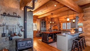 Una cocina rústica con estufa de leña, paredes de piedra y una isla grande con taburetes.