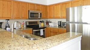 Una cocina con armarios de madera, un refrigerador de acero inoxidable, un microondas, una estufa y una encimera de granito.