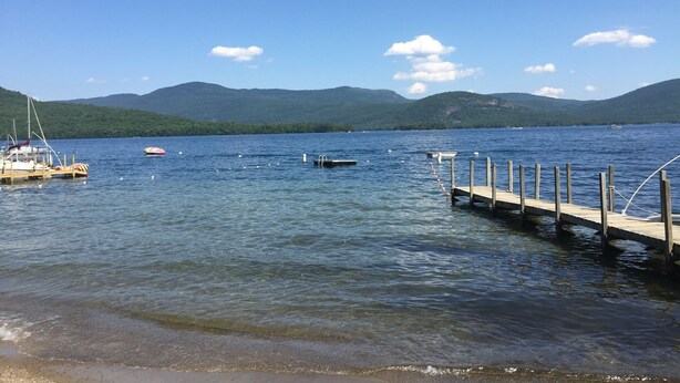 Un lago tranquilo con barcos amarrados a un muelle, rodeado de montañas.
