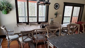 Un comedor con una mesa y sillas de madera, una encimera de cocina y un ventanal con vistas a árboles.