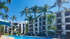 Ein Resort mit Swimmingpool, Palmen und einem mehrstöckigen Gebäude mit Balkonen.