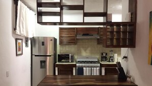 Eine kompakte Küche mit einem Edelstahl-Kühlschrank, einer eingebauten Mikrowelle, einem Herd und einer Kaffeemaschine. Es gibt drei Hocker an der Arbeitsplatte.