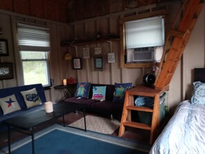 En mysig stuga med träpanel på insidan, en soffa med färgglada kuddar, ett litet bord och en stege som står lutad mot väggen.