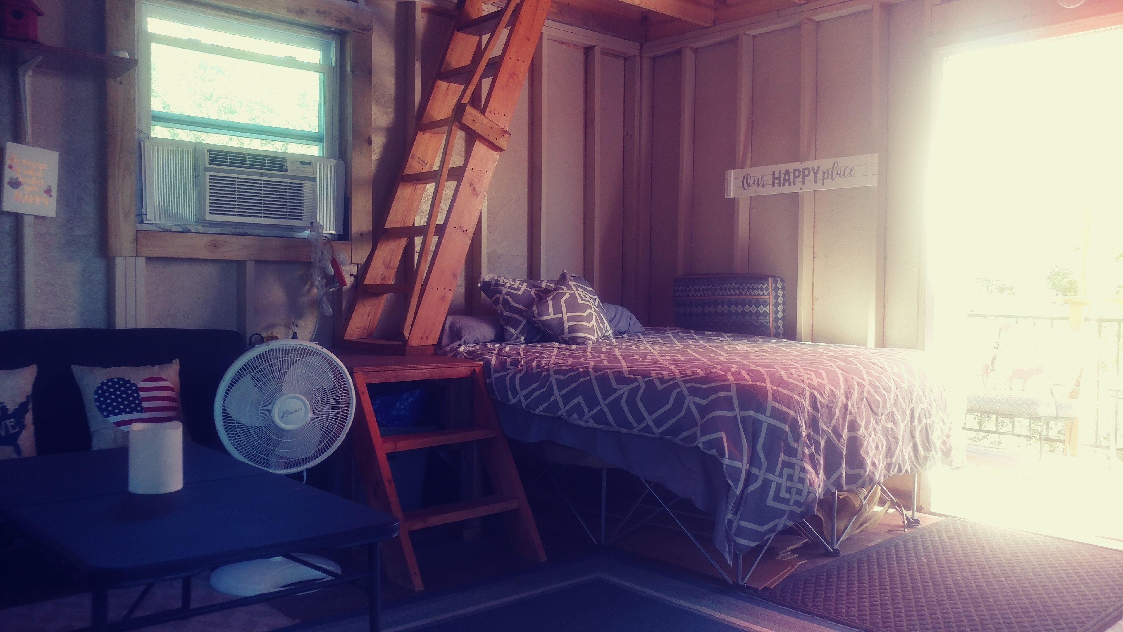 Une pièce confortable avec un lit, un bureau, une échelle, un ventilateur et une pancarte sur laquelle on peut lire : « Notre havre de paix ».