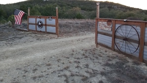 Una rústica puerta de madera con una rueda de carretilla antigua, un letrero de ‘prohibido el paso’ y una bandera estadounidense.