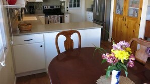 Une cuisine avec des meubles blancs, un réfrigérateur en acier inoxydable et une table à manger en bois, accompagnée de chaises.