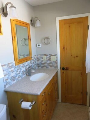 A bathroom with a wooden vanity, a white sink, a mirror, and a towel hanging on the door. - Green Creek Retreat- Pet Friendly Family Retreat, On the Way to Yellowstone! (Cody)