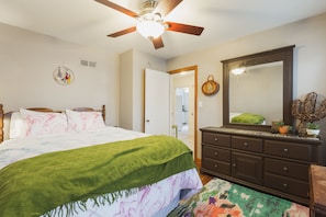 A bedroom with a bed, dresser, ceiling fan, and a door leading to another room.