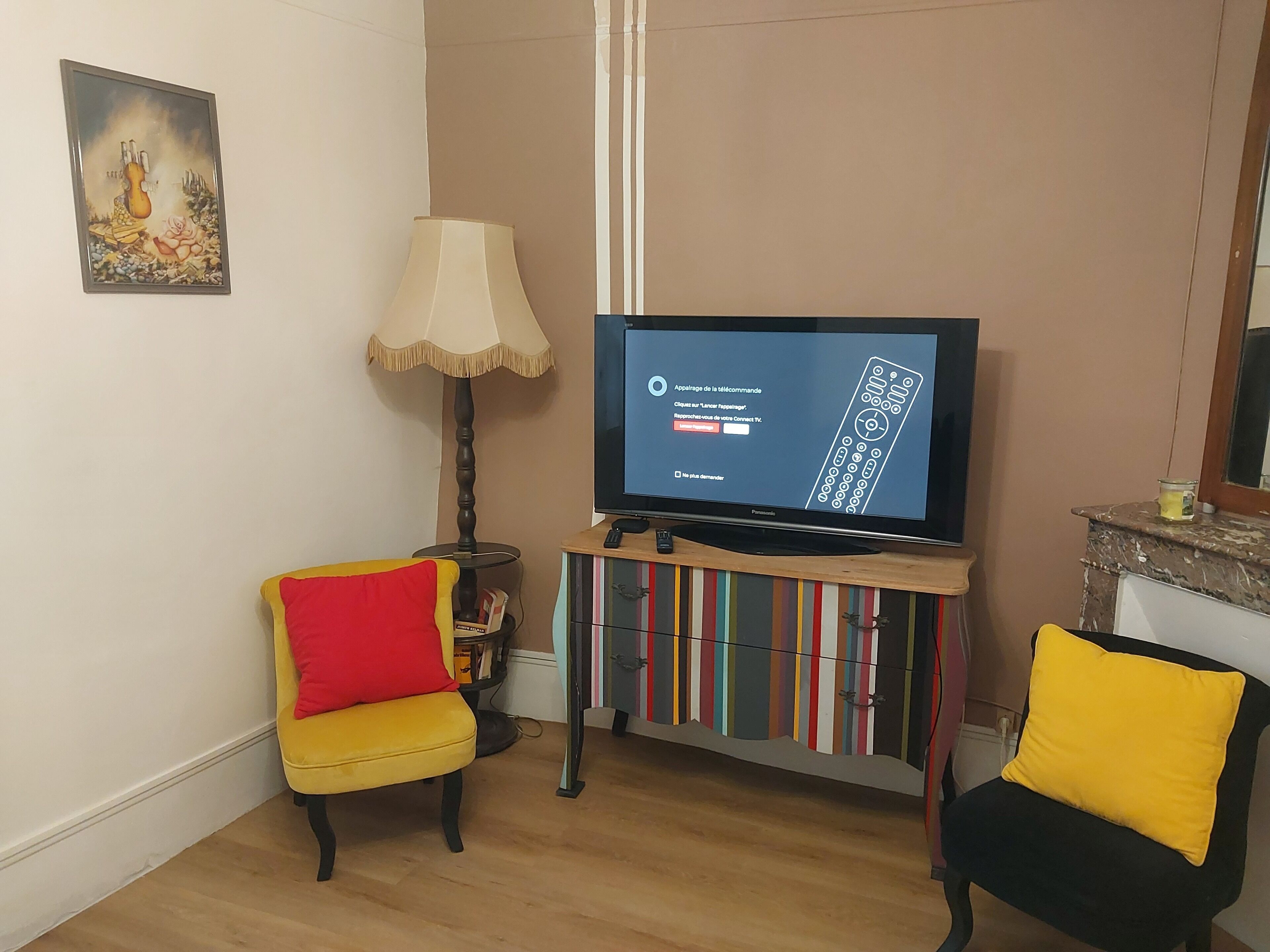 Una sala de estar con televisor sobre un mueble bajo, una lámpara, una silla con cojín rojo y una estantería.