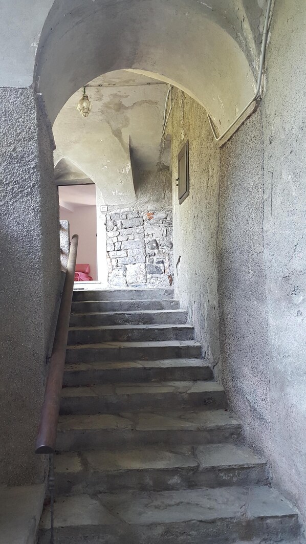 Un escalier en pierre mène à une pièce dont un des murs est également en pierre et qui possède une fenêtre.