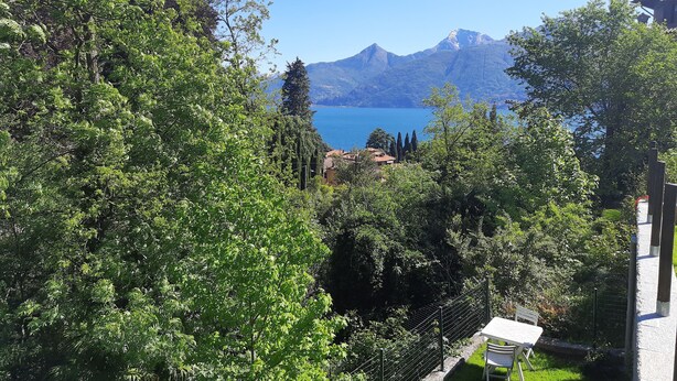 Blick auf eine Berglandschaft mit einem See, umgeben von üppigem Grün und einem Gebäude mit weißer Fassade.
