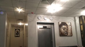 Eine Lobby mit einer Rezeption, einer schwarzen Ledersofa, einer an der Wand befestigten Buddha-Statue und einer Uhr.