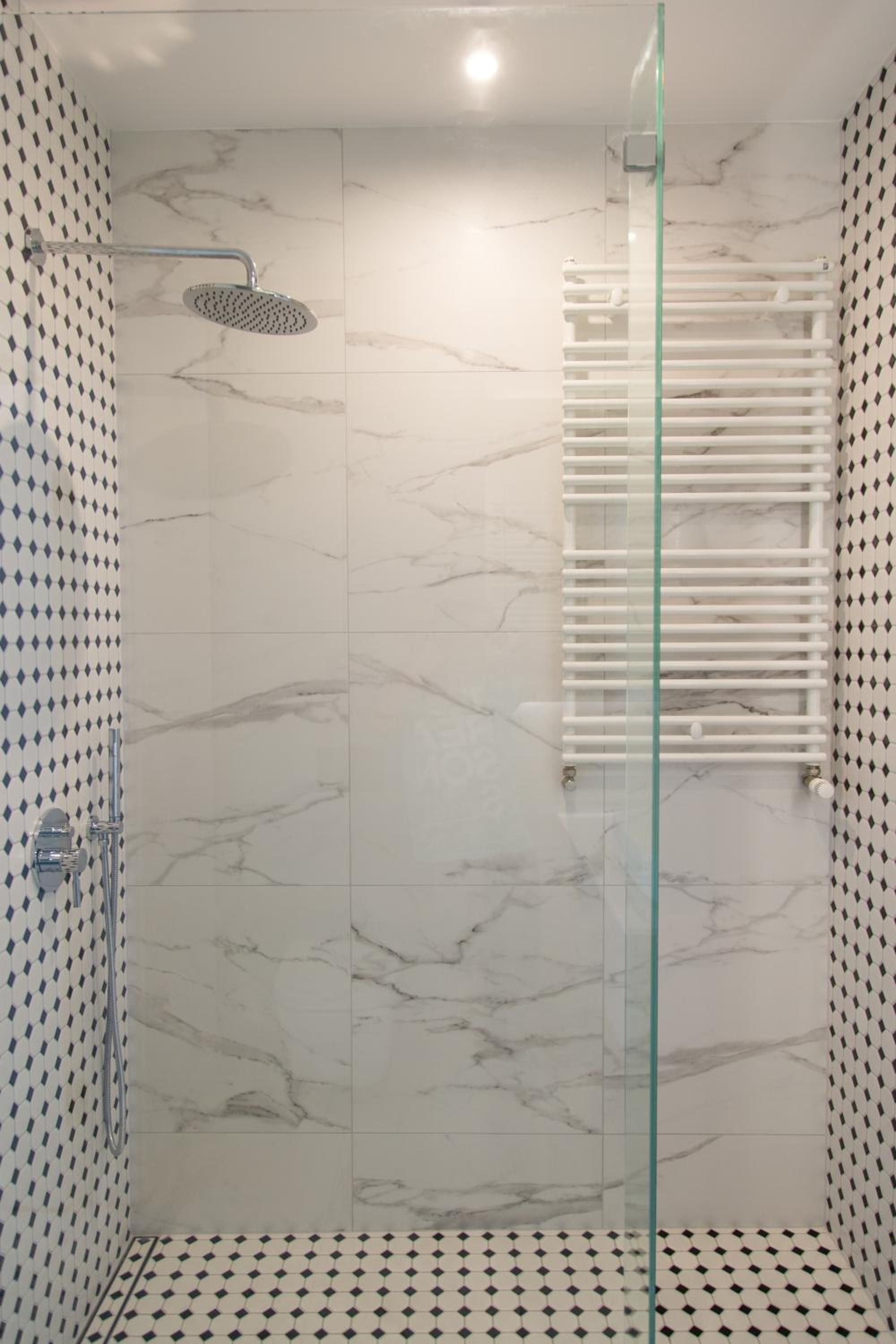 A modern bathroom with a glass shower enclosure, white marble tiles, and a patterned wall design.