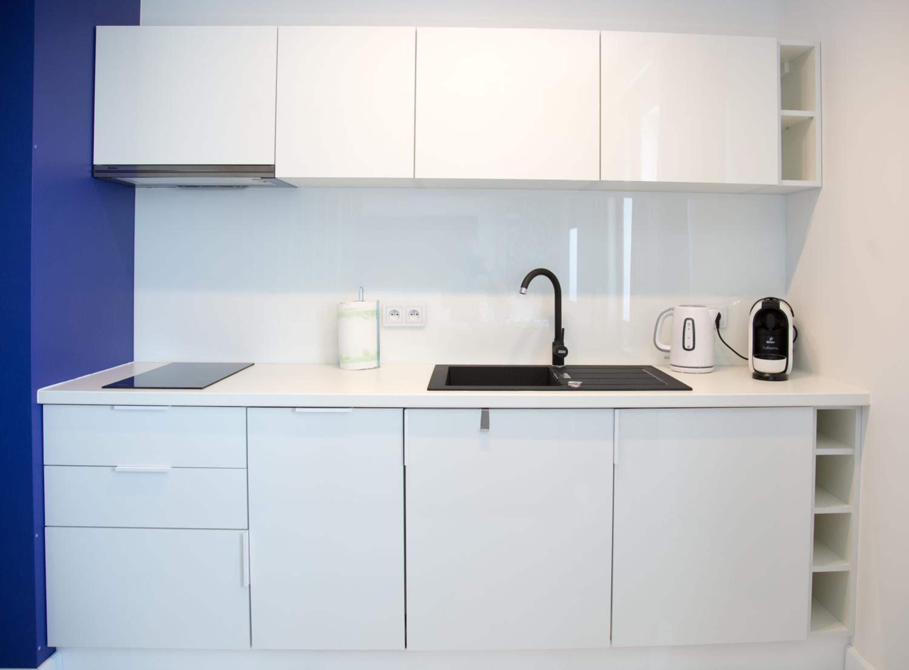 A modern kitchen with white cabinets, a black sink, a kettle, and a coffee maker.