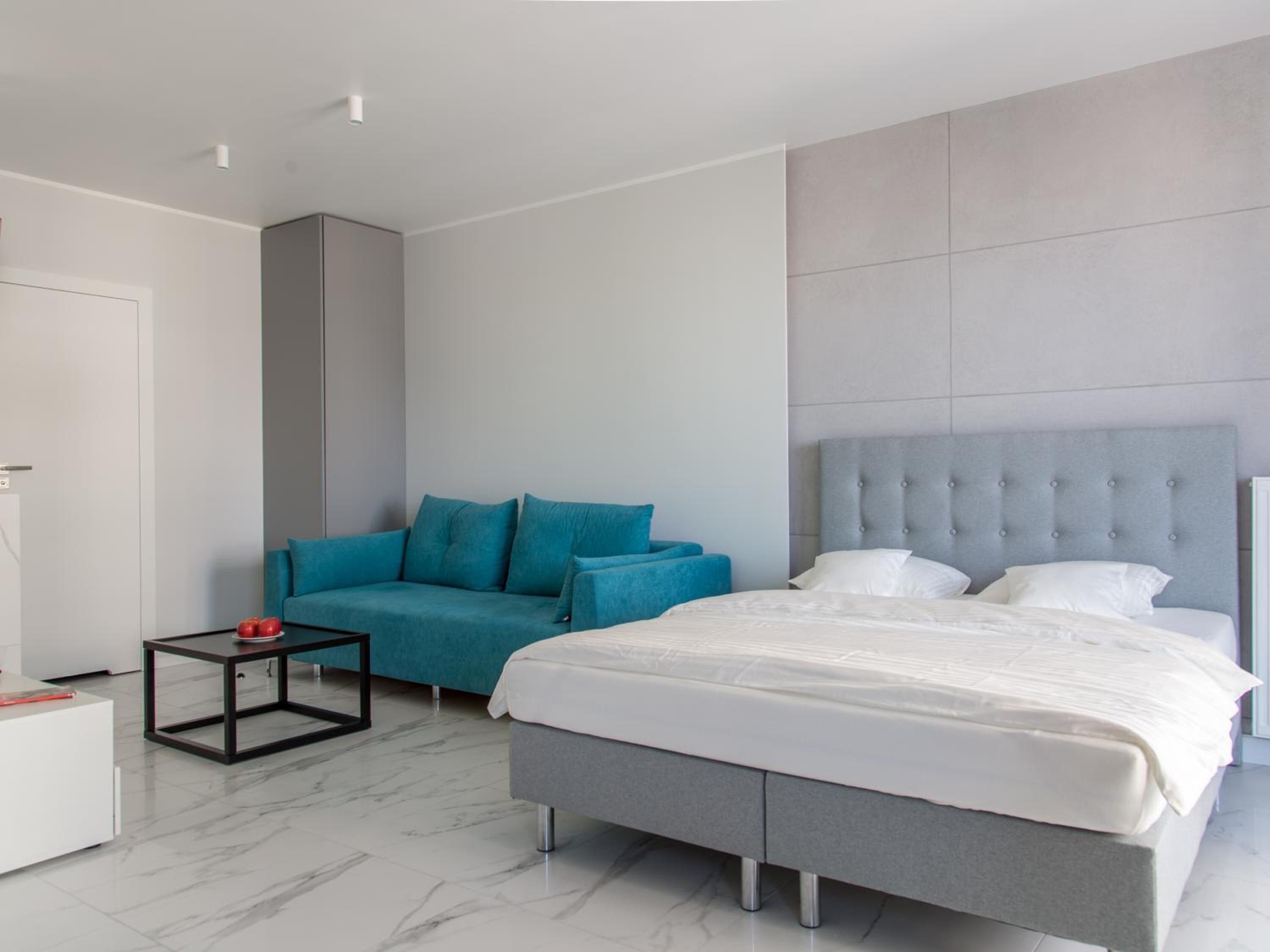 A modern hotel room with a large bed, a sofa, a small table, and a white wardrobe.