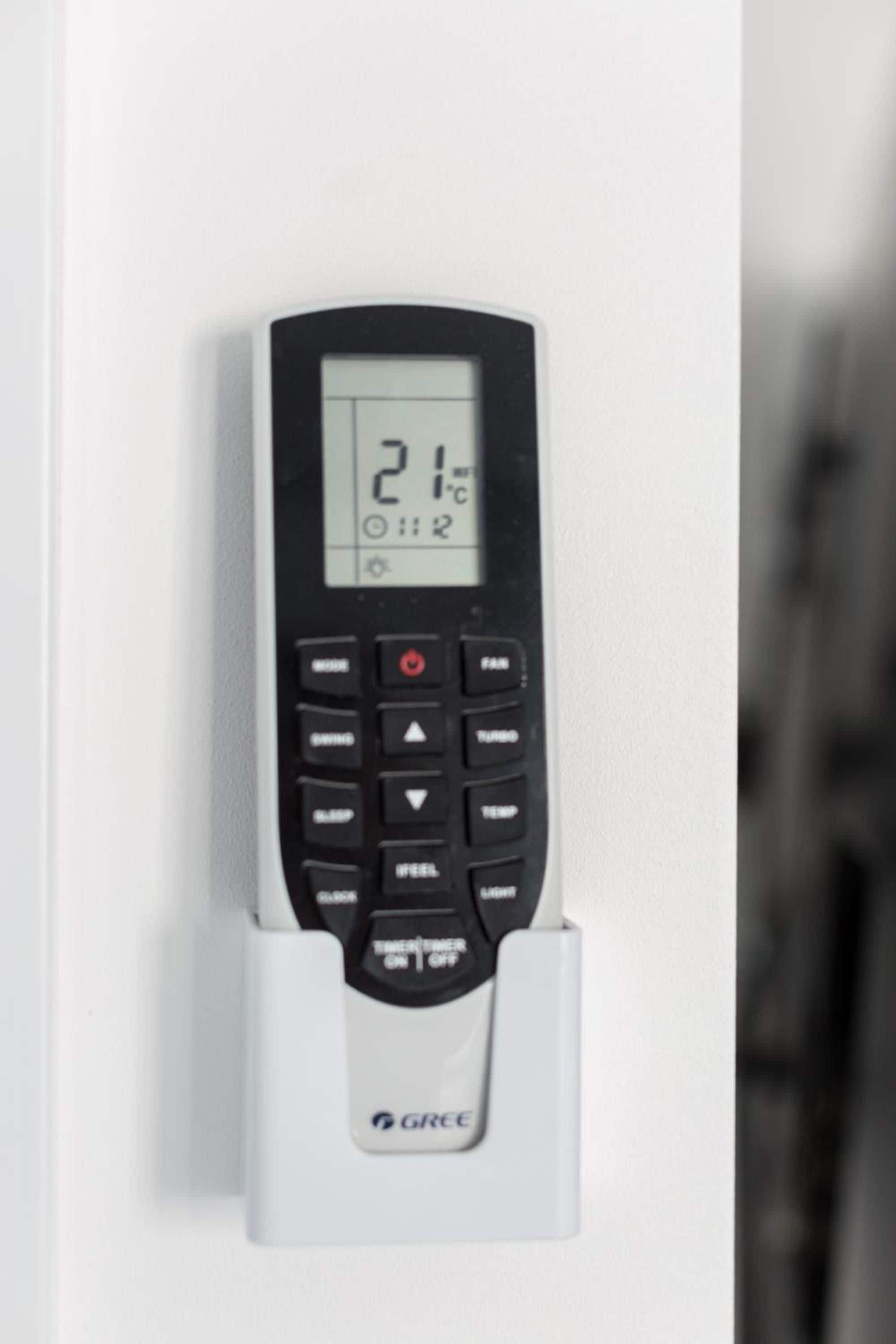 A GRCE branded electronic device mounted on a white wall, displaying a temperature of 21 degrees Celsius and a time of 12:02.