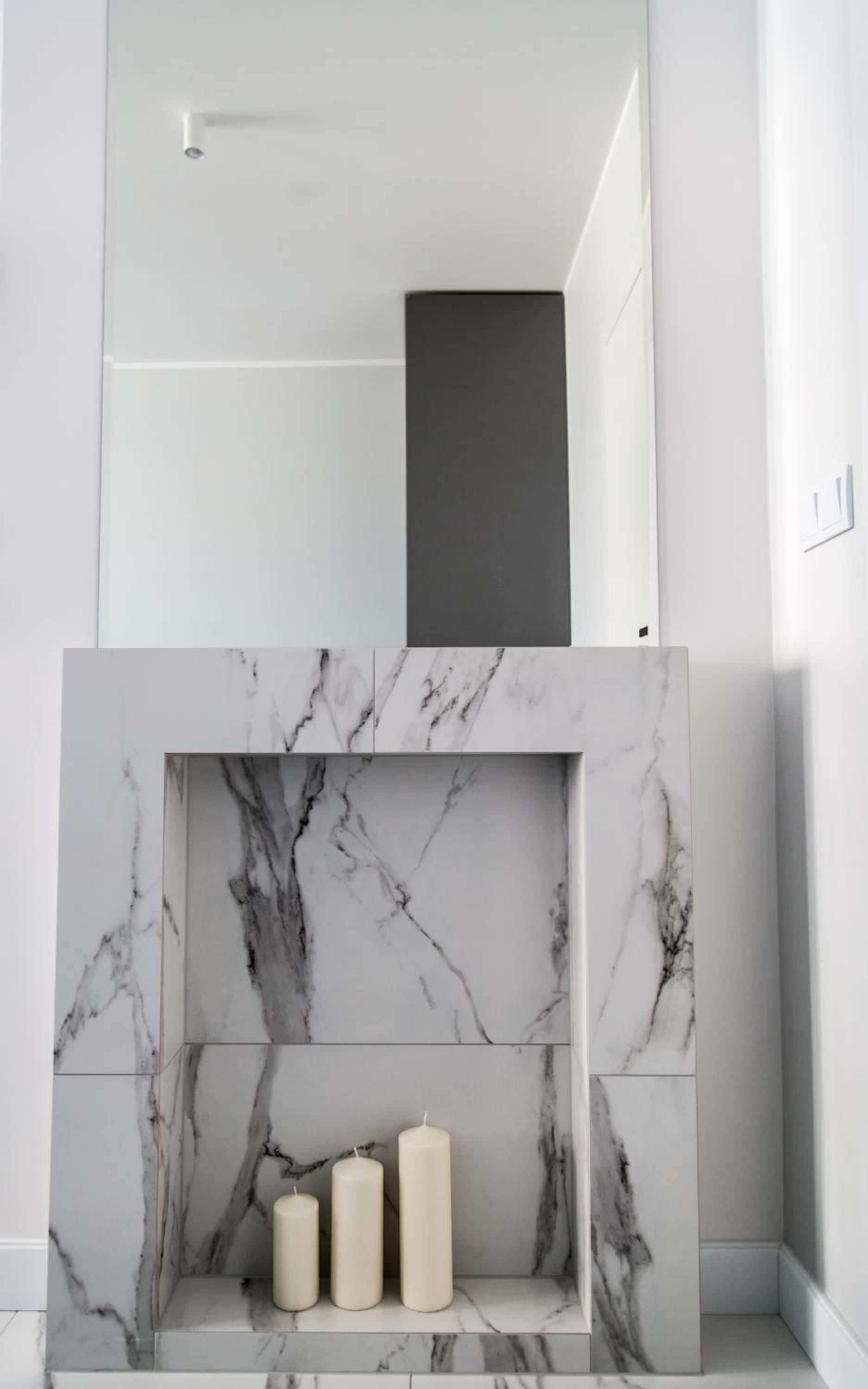 A modern bathroom with a marble vanity, a dark shelf, and three candles.