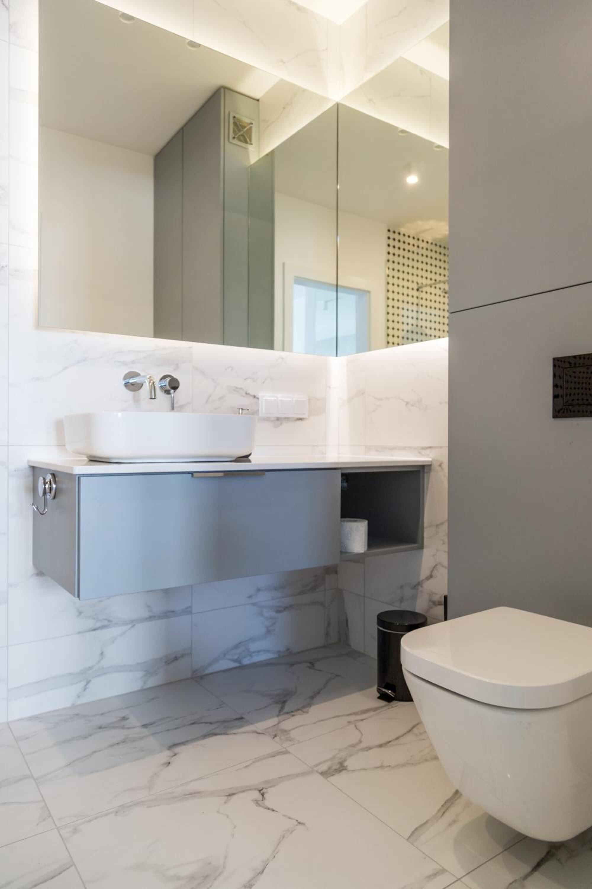 A modern bathroom with a marble sink, a toilet, and a glass-enclosed shower.