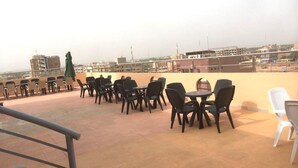 Eine Dachterrasse mit Außenbestuhlung, darunter Tische und Stühle, und Blick auf die Skyline im Hintergrund.