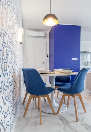 A modern dining area with a round table, four blue chairs, and a pendant light.