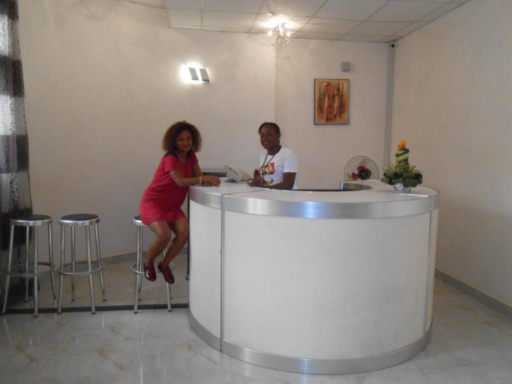 A reception desk with a person seated behind it, a counter, and two stools to the left.
