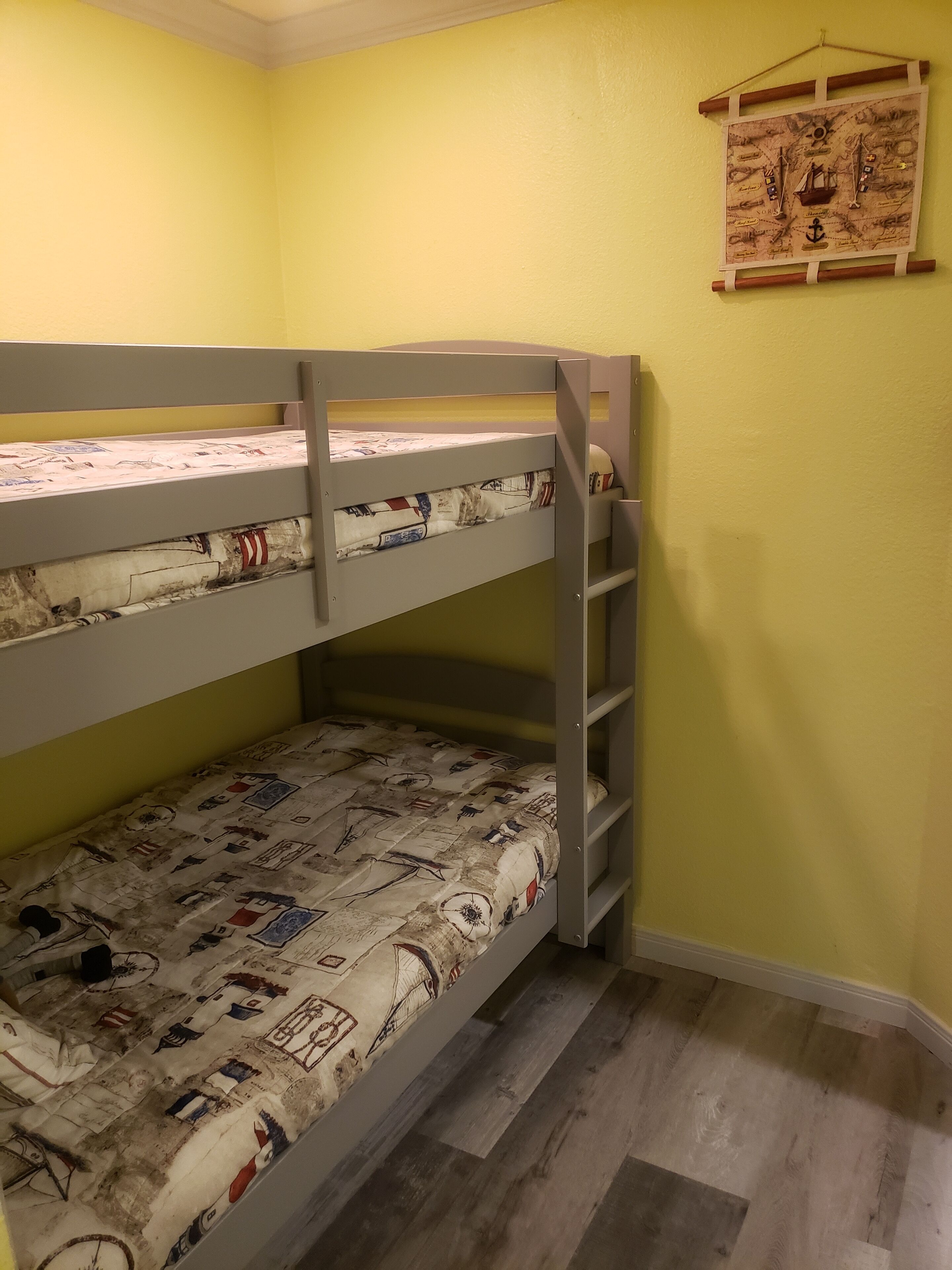 A bunk bed with a nautical-themed mattress, a wooden headboard, and a wall-mounted map.