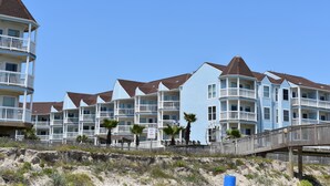 Hotel na orla marítima com várias varandas, um deck de madeira e uma placa indicando acesso à praia.