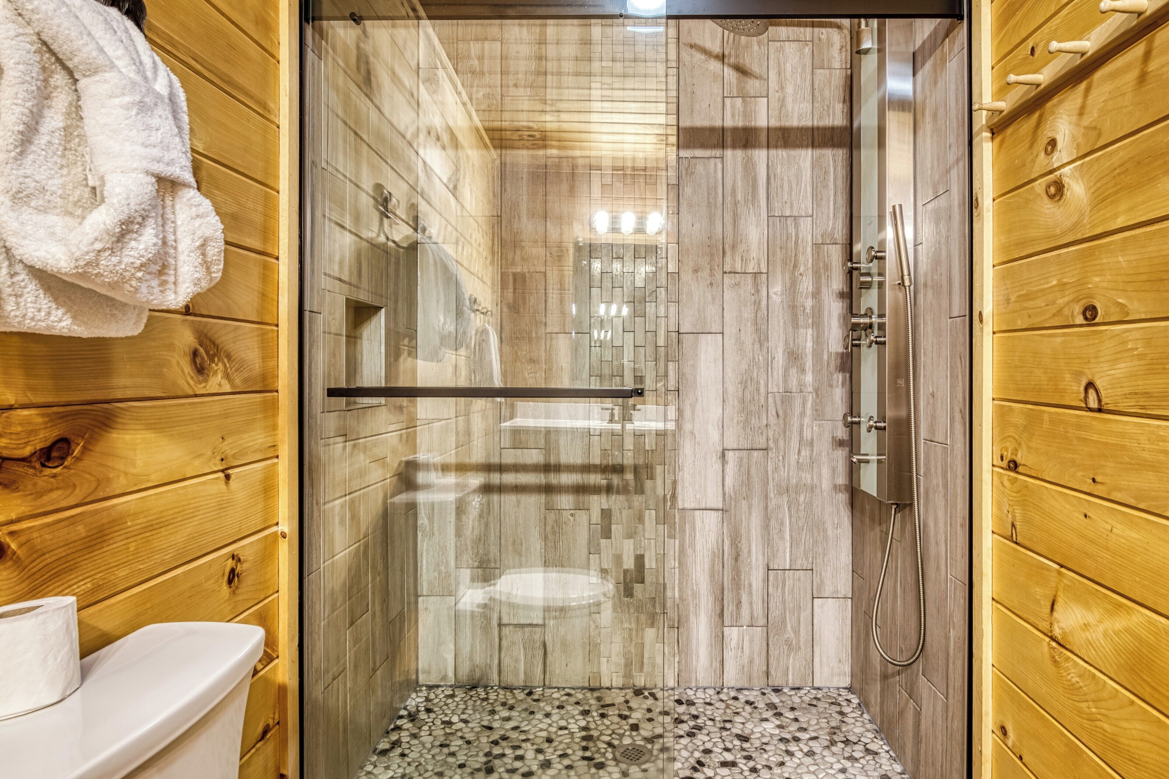 A wooden-paneled bathroom with a glass-enclosed shower, a toilet, and a towel rack.