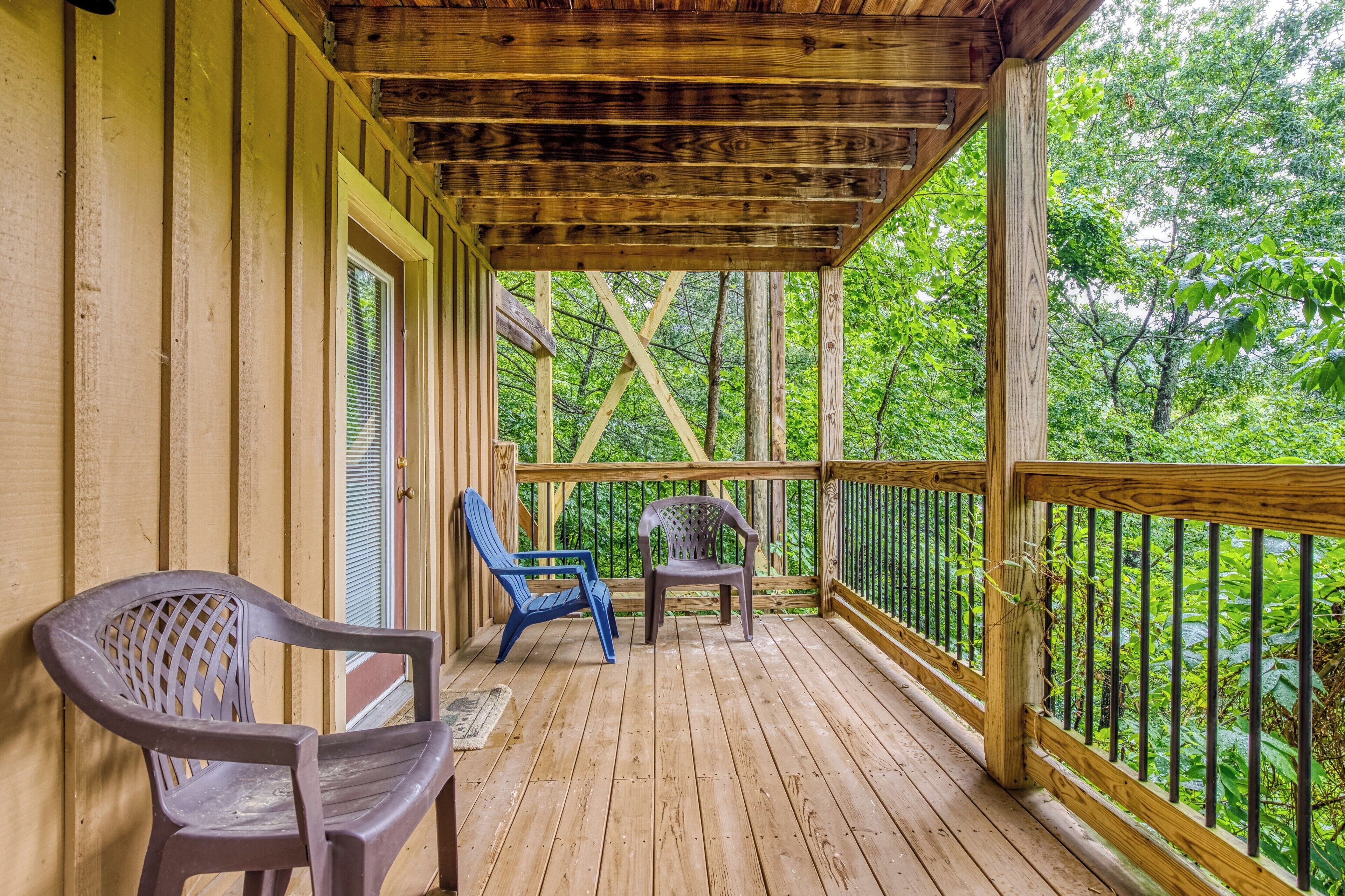 A wooden deck with two plastic chairs, a wooden railing, and a view of a forest.