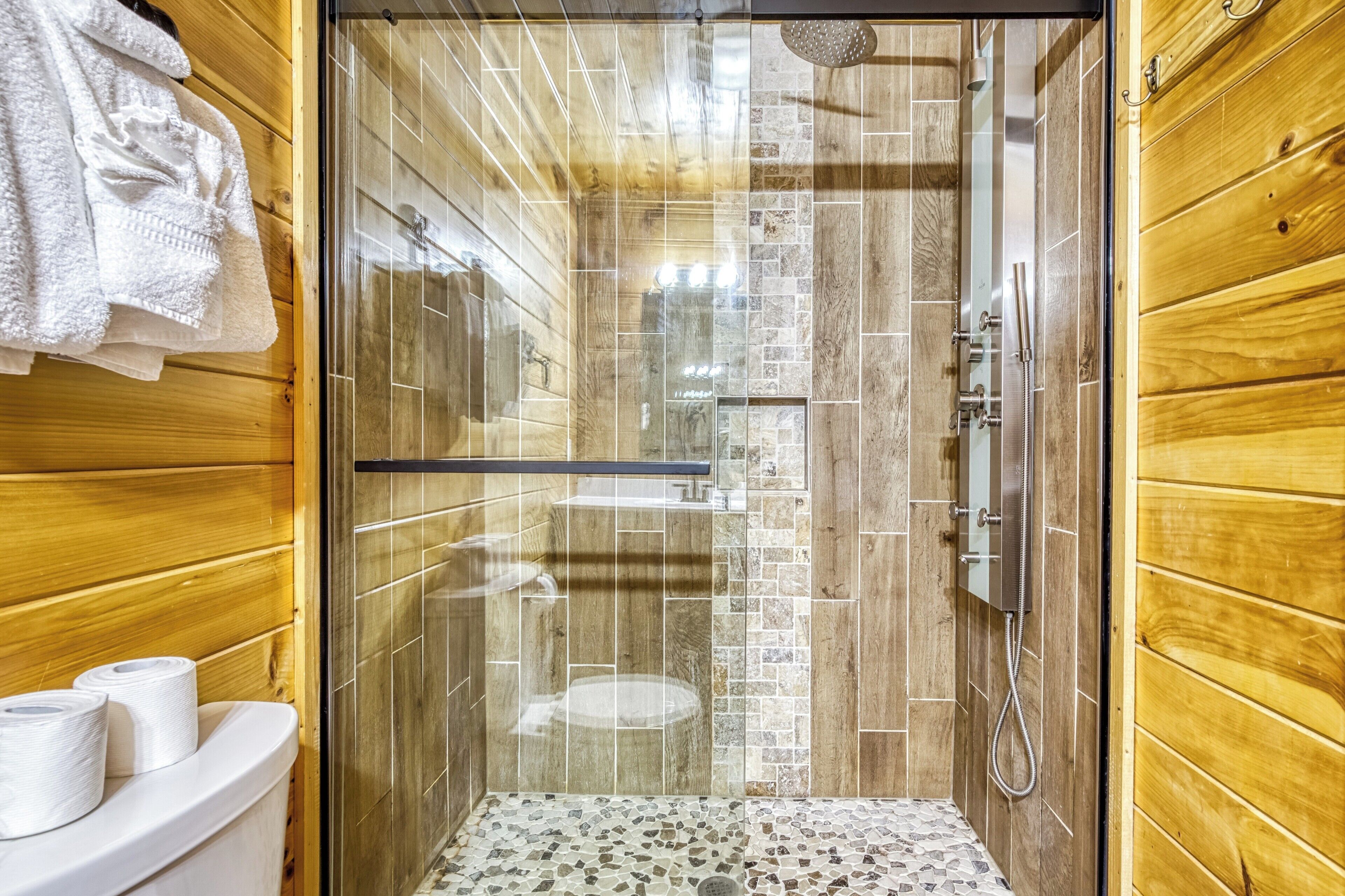 A shower with a glass door, a toilet with a white seat, and a wooden wall.