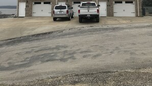 Un edificio de varios pisos con tres garajes, dos camiones estacionados y vista al agua de fondo.