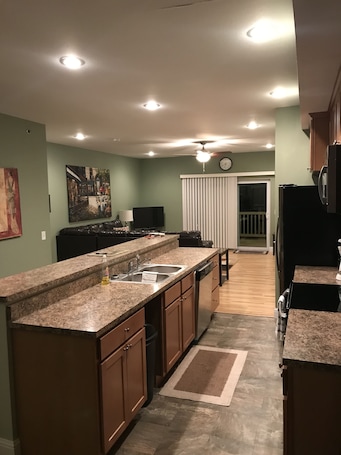 A modern kitchen with granite countertops, a dishwasher, and a large window with blinds.