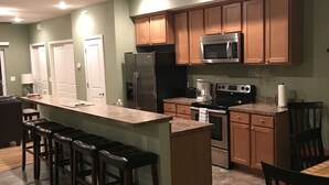 Una cocina moderna con armarios de madera, una isla central con taburetes de bar, microondas, refrigerador y cafetera.