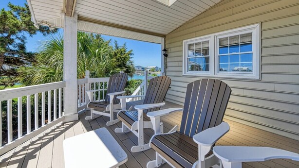 A covered porch with Adirondack chairs and a table, overlooking a body of water and greenery. - Pop's Place in the private gated community of Inlet Harbour (Garden City Beach)
